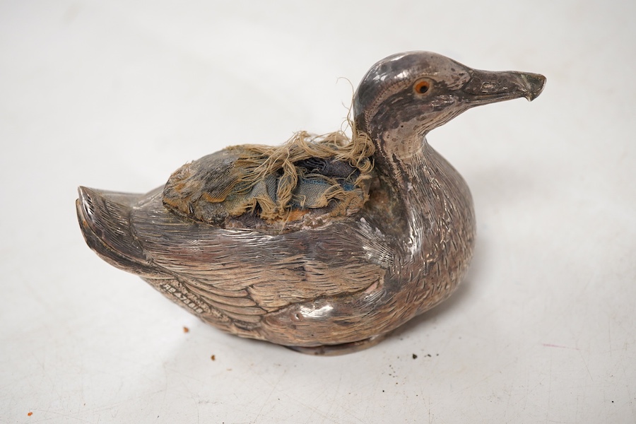 An Edwardian novelty silver mounted pin cushion, modelled as a duck, by Abrahall & Bint, engraved with 'feather' decoration and glass eyes, Birmingham, 1906, length 94mm, height 59mm(a.f.).